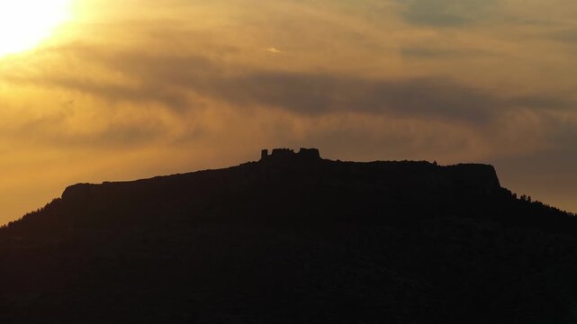 A dramatic silhouette of ancient ruins atop a hill is seen against a vivid sunset sky in Opoul Perillos, France.