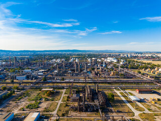 Fototapeta premium Industrial site viewed from above shows complex structures and machinery under a clear sky with distant city in the background during daytime