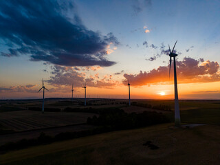 Obraz premium Wind turbines stand tall as the sun sets over the horizon, casting a warm glow across the landscape in a rural setting
