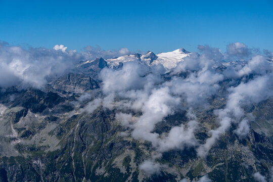 dramatic alpine mountain range with rugged peaks emerging through low clouds under a clear blue sky