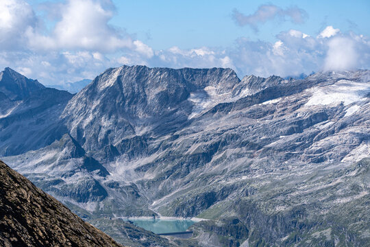 dramatic alpine mountain range with rocky peaks, glaciers and clouds under a blue summer sky