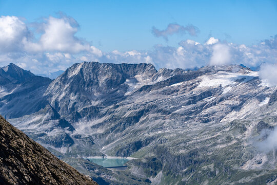 dramatic alpine mountain range with rugged rocky peaks, glaciers and clouds under a blue summer sky