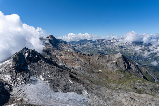 panoramic view of rugged alpine mountain peaks and rocky highlands beneath dramatic clouds and blue sky