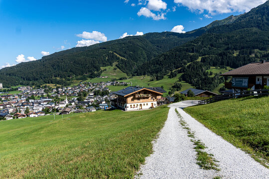 gravel country road leading through green alpine meadows toward a scenic mountain village