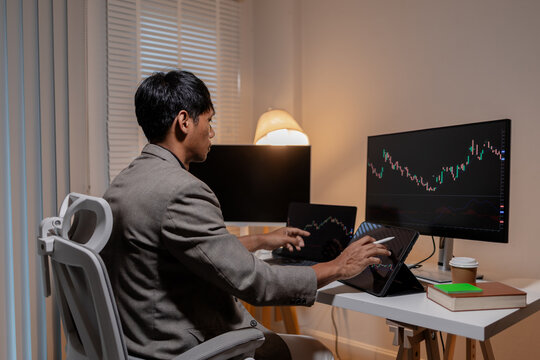 Professional trader analyzing stock market charts across multiple screens using laptop and tablet to monitor price movements, technical indicators and investment strategies in modern trading workspace