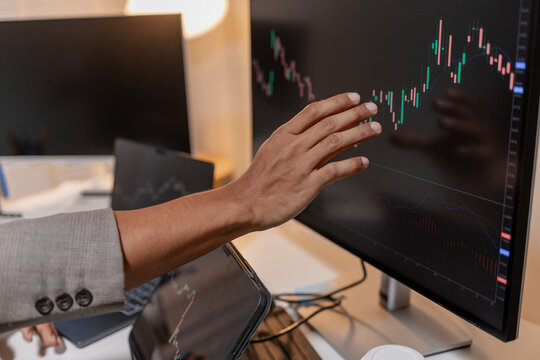 Professional trader analyzing stock market charts across multiple screens using laptop and tablet to monitor price movements, technical indicators and investment strategies in modern trading workspace