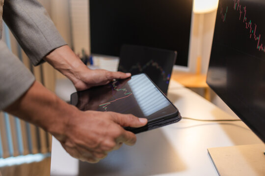 Professional financial analyst reviewing stock market charts across multiple screens using a tablet, laptop and calculator to evaluate price movements, technical indicators, and investment strategies.