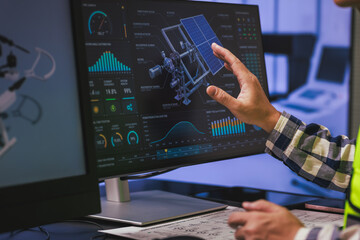 Fototapeta na wymiar Hand points at a computer screen with a satellite model and data charts, space technology analysis and engineering work.