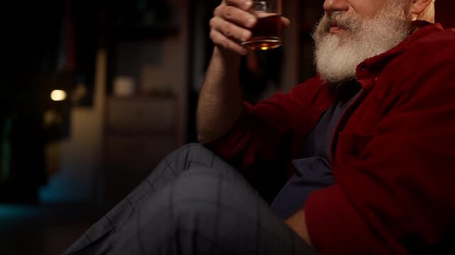 Middle-aged bearded man drinks whiskey on the floor, facing emotional burnout