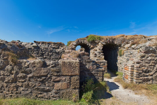 Weathered stone ruins with multiple arched openings and rough walls stand against a clear blue sky - Jacob's Mine, Botallack, Cornwall, UK