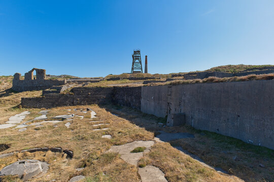 A historic mining landscape under a clear blue sky. Weathered ruins and dry grass are in the foreground, with a tall - Jacob's Mine, Botallack, Cornwall, UK