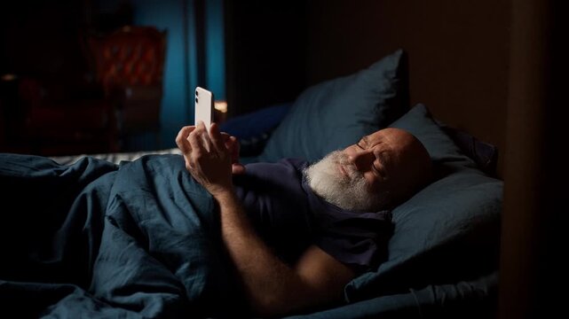 Lonely bearded man in his 50s scrolls on phone while lying awake with insomnia
