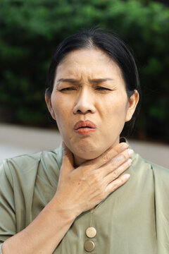 middle aged asian female suffering from cough and cold symptoms outdoors, weak and unwell