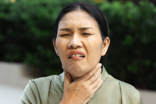 middle aged asian female suffering from cough and cold symptoms outdoors, weak and unwell
