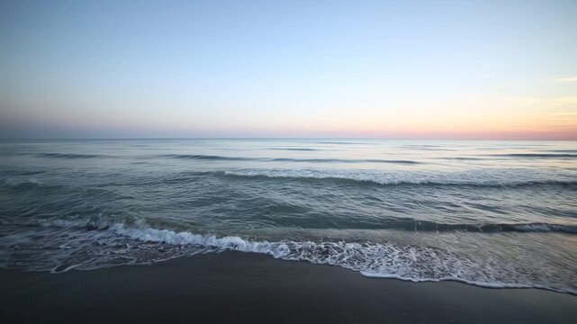 Gentle ocean waves rolling onto a quiet sandy beach at sunset with soft pastel sky