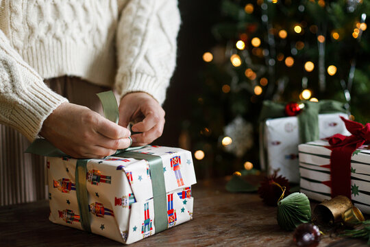 Woman hands wrapping Christmas gift box on rustic table, concept of winter DIY, creative present packaging, and festive seasonal preparation. Happy holidays