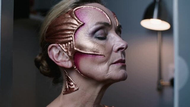 Widening camera revealing woman relaxing in profile backstage in costume, showing prosthetic makeup