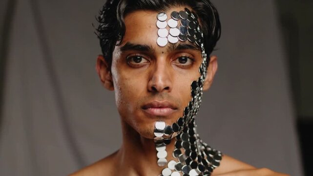 Responding to cue, bare-chested male model turning to face camera at studio, with reflective discs