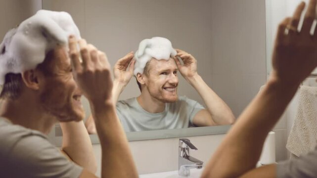 Cheerful man having fun shaping soap foam into bunny ears on his head in playful moment
