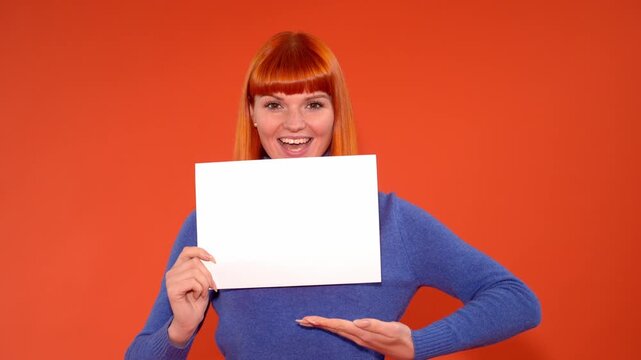 Cheerful woman shows blank sign with bright orange background at a studio