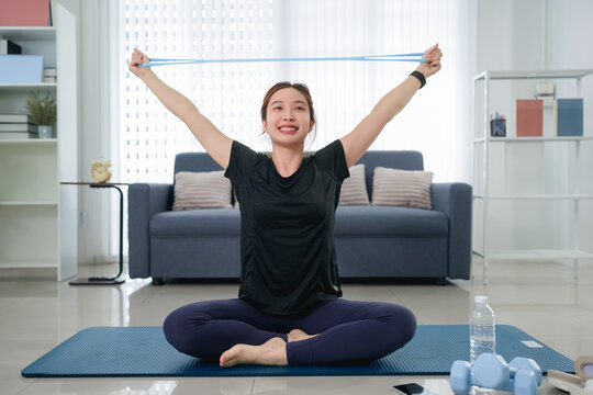 Young Asian woman stretching with resistance band during yoga session on mat in bright living room