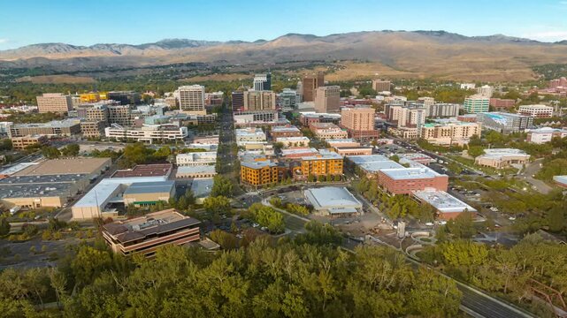 Aerial view of the downtown Boise skyline with modern buildings, urban streets, and surrounding foothills under a clear blue sky in Boise, Idaho, United States.