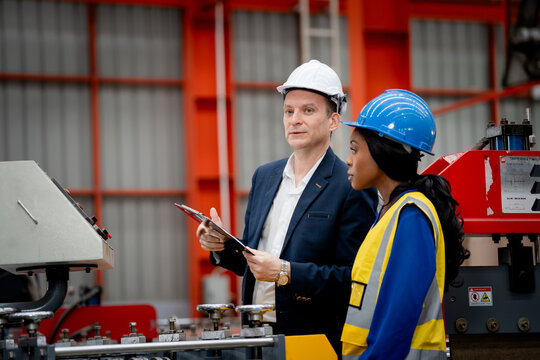 two professional engineer, worker, technician use clipboard discuss work, walk in steel metal manufacture factory plant industry. man and woman wear hard hat check quality machine