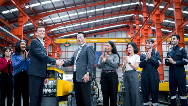 Business partnership in manufacturing. Executives and factory professionals celebrate a successful handshake inside an industrial plant. Partnership, teamwork, leadership, industry, success