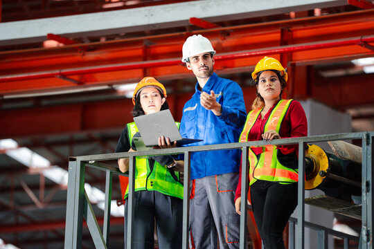 Industrial teamwork and digital manufacturing. Engineers review production data using a laptop and tablet beside factory machinery. Industry, teamwork, technology, inspection, production