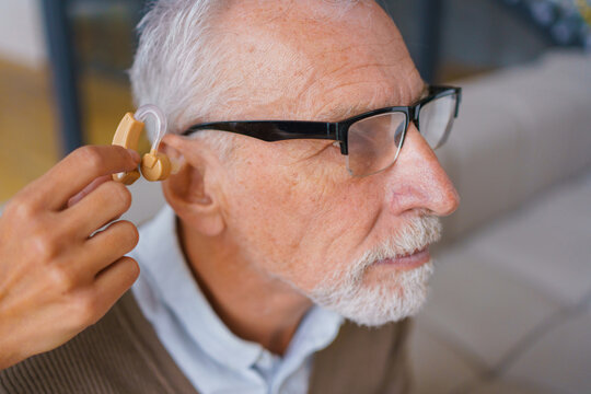 Female hand holding hearing aid with senior man close up of hearing assistance listening device, elderly care, audiology support and healthcare rehabilitation concept
