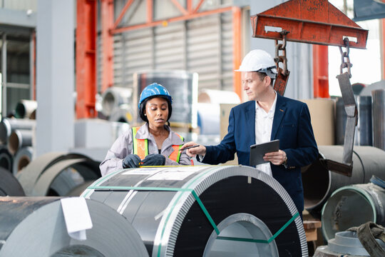 professional engineer,worker,technician use clipboard discuss work, walk in steel metal manufacture factory plant industry. Black African American man and woman wear hard hat check quality machine.