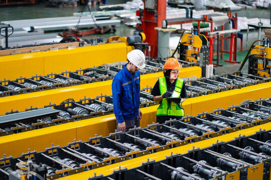 professional engineer,worker,technician use clipboard discuss work, walk in steel metal manufacture factory plant industry. Black African American man and woman wear hard hat check quality machine.