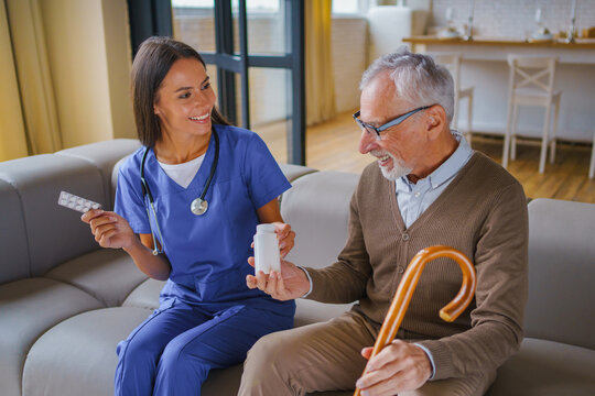Young female nurse handing pill jar to elderly man at home, caregiver supporting senior patient with medication, healthcare service and home care concept