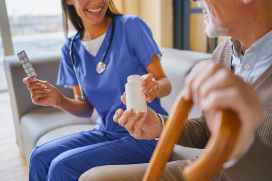 Close up of young female nurse handing pill jar to elderly man at home, caregiver supporting senior patient with medication, healthcare service and home care concept