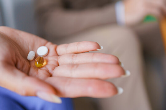 Female hands holding tablets and capsules with senior man in background, close up of medication and elderly patient, healthcare treatment, home care service and senior support concept