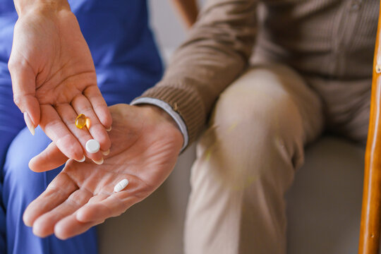 Close up of nurse giving tablets and capsules to senior man's hand, caregiver assisting elderly patient with medication, healthcare support, treatment, home care service and senior care concept