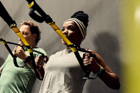 Two diverse people doing TRX suspension training in gym showing fitness focus and strength together