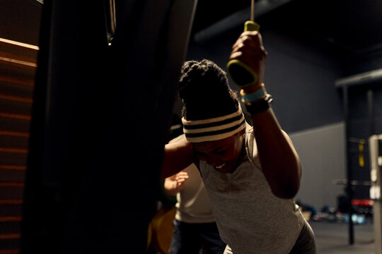 Focused black woman training on a cable machine in a dimly lit gym during an intense workout session