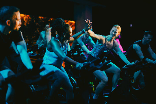 Happy diverse group high-fiving during an energetic indoor cycling class at a night fitness studio