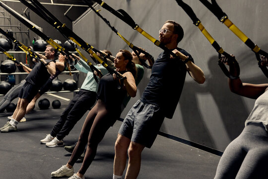 Diverse fitness group class doing TRX suspension training in gym showing teamwork and determination