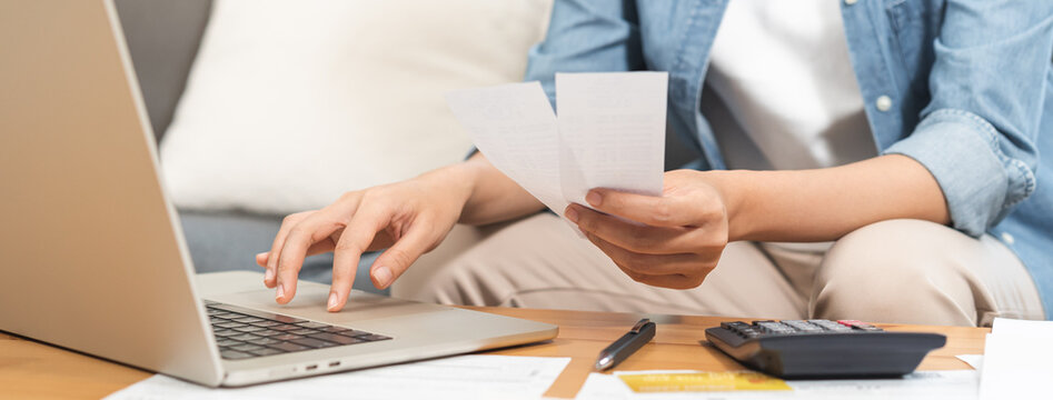 Close up of a person hand holding receipts while using laptop and calculator for home budget planning, financial management, monthly expense tracking and tax calculation