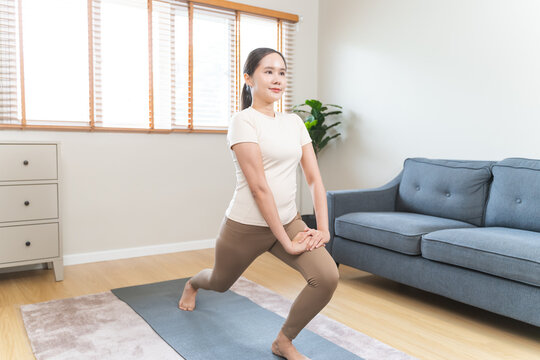 Healthy asian young woman practicing lunge stretching exercise on mat at home living room for legs strength training fitness workout and wellness lifestyle self care building