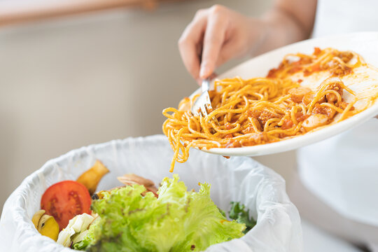 Compost from leftover food asian young housekeeper woman, female hand holding spaghetti plate use fork scraping waste, food throwing away into garbage, trash or bin. Environmentally responsible.