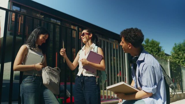 Happy high school students interact while sharing items and laughing together on campus. Friends enjoy a lively discussion outdoors, exchanging school supplies with smiles.