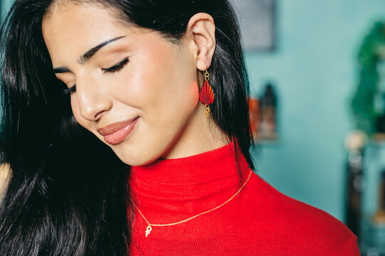 Portrait of a smiling woman in a red turtleneck with red earrings and a gold necklace