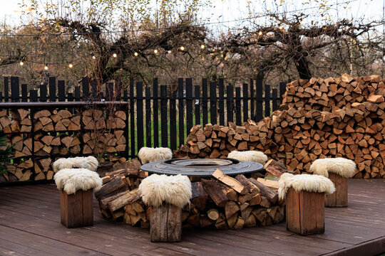 Wooden seating around fire pit in outdoor area with stacked logs and trees