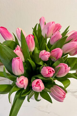 Fototapeta premium Bouquet of pink tulips arranged on a table with green leaves