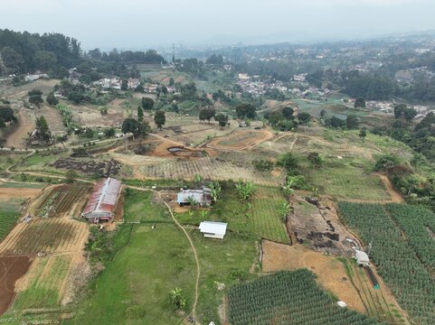 Aerial view of the Ciloto area featuring terraced agricultural fields, small rural houses with metal roofs, and lush hilly terrain in Cipanas, West Java, Indonesia.
