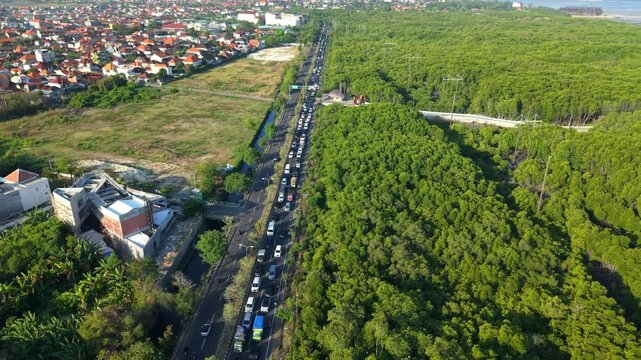 Aerial view of heavy traffic congestion on the Ngurah Rai Bypass Road, flanked by dense mangrove forest and residential areas in Kecamatan Denpasar Selatan, Bali, Indonesia.
