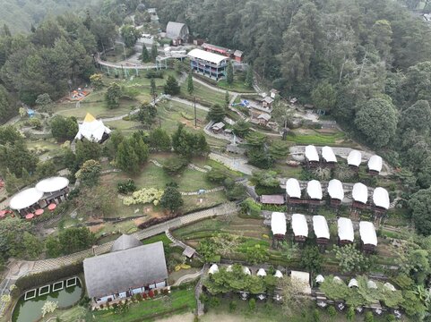 Aerial view of the Ciloto area in Cipanas, featuring lush green hills, terraced landscapes, small resort buildings with white roofs, and winding pathways in Cipanas, West Java, Indonesia.